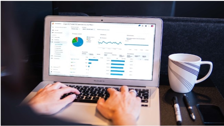 A laptop with someone typing showing a data visualization dashboard with a mug and pens alongside it.